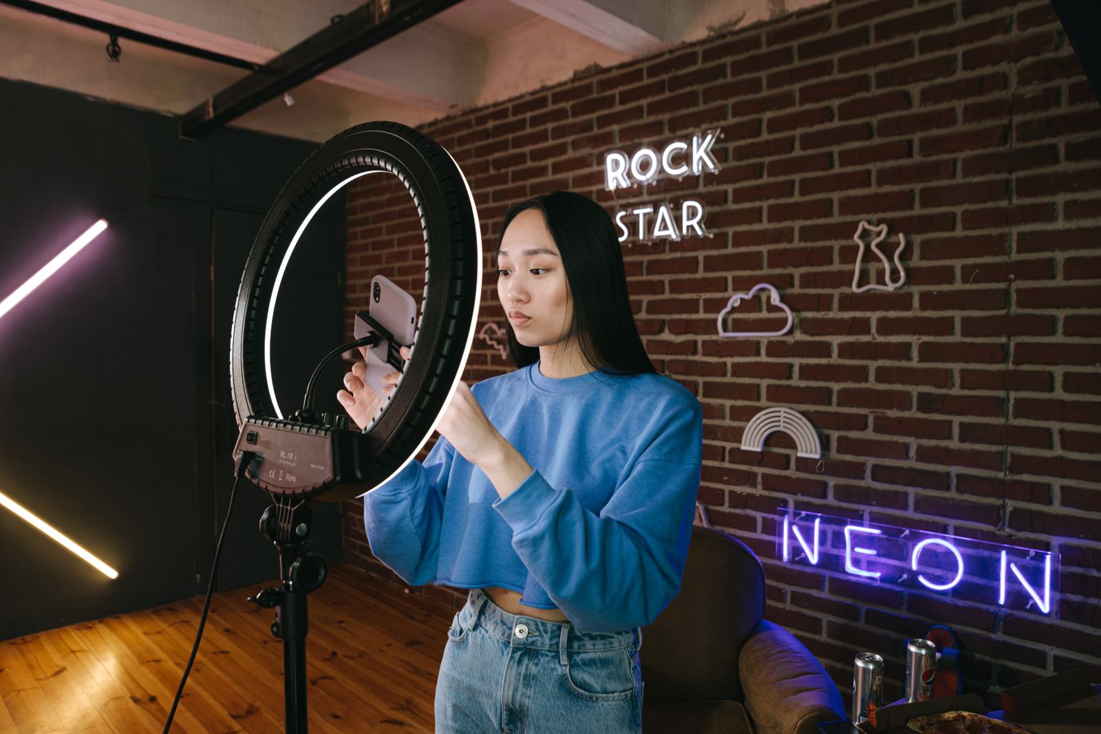 Content creator adjusting her phone on a ring light against a neon-sign wall